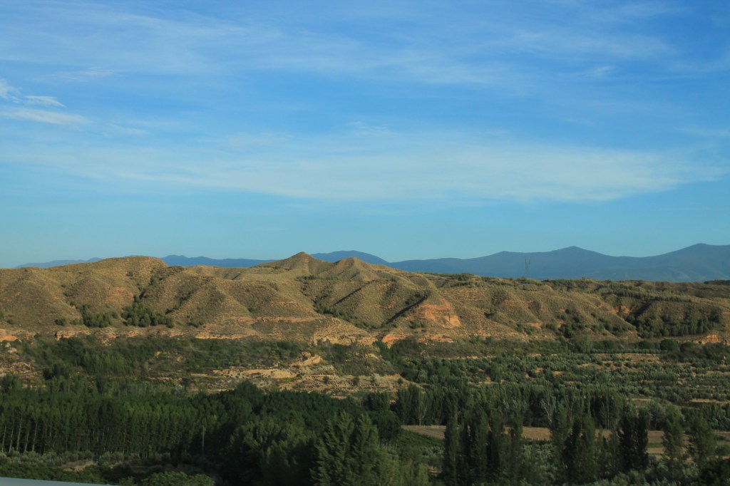 brown foothills against blue sky with mountains in the distance