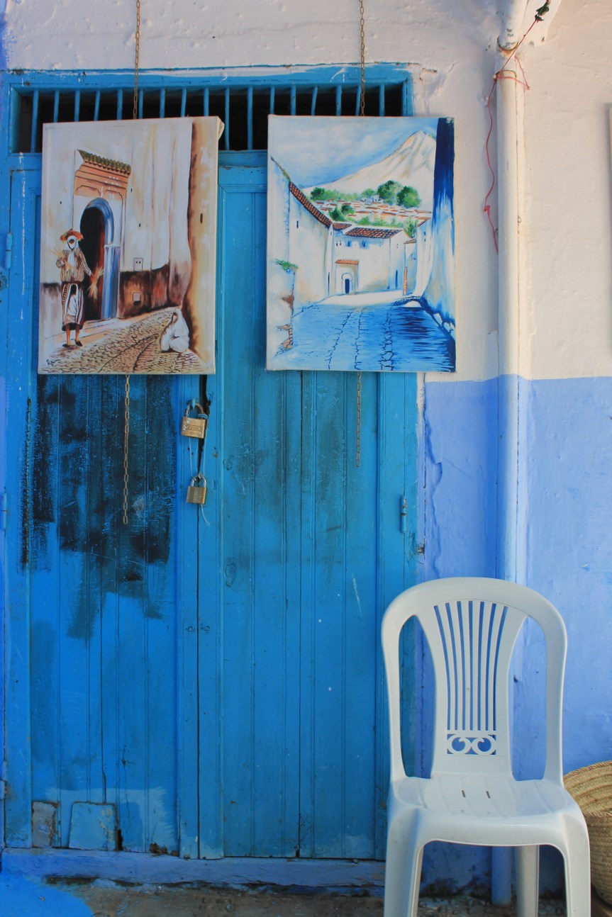 paintings hanging on blue wall next to white plastic chair