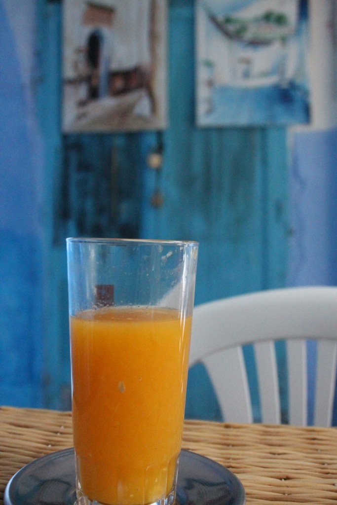 glass of orange juice on wicker table next to blue wall